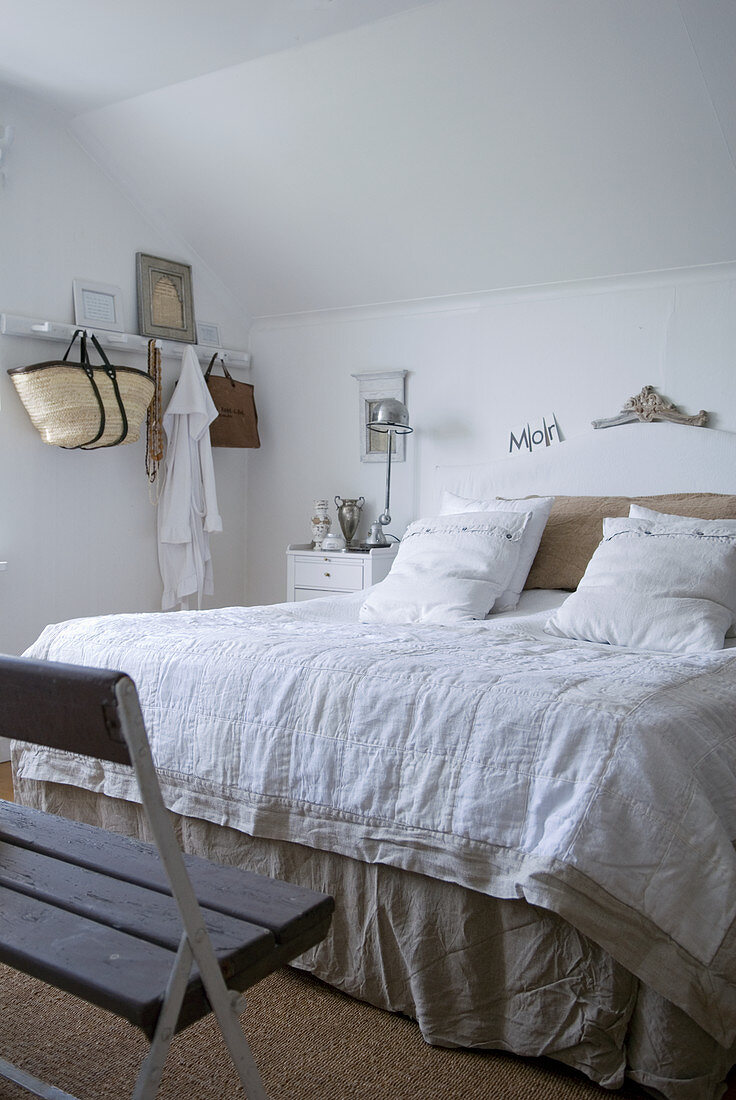 Doppelbett mit Leinenbettwäsche in Schlafzimmer mit rustikaler Holzbank und weißer Hakenleiste