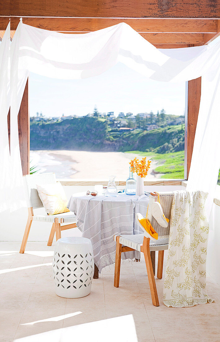 Runder Tisch mit zwei Stühlen auf der Terrasse mit Sonnenschutz und Blick auf das Meer