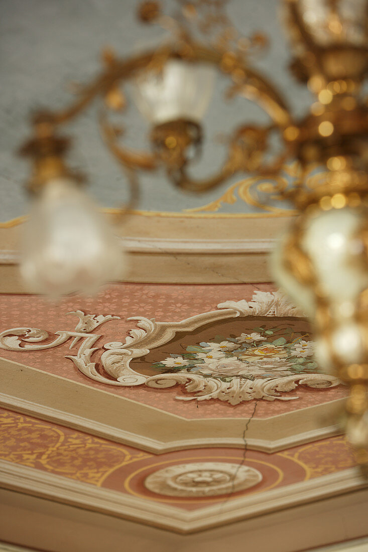 Blick von unten auf Deckenkerzenleuchter aus Gold und bemalte Wand mit Stuckarbeit