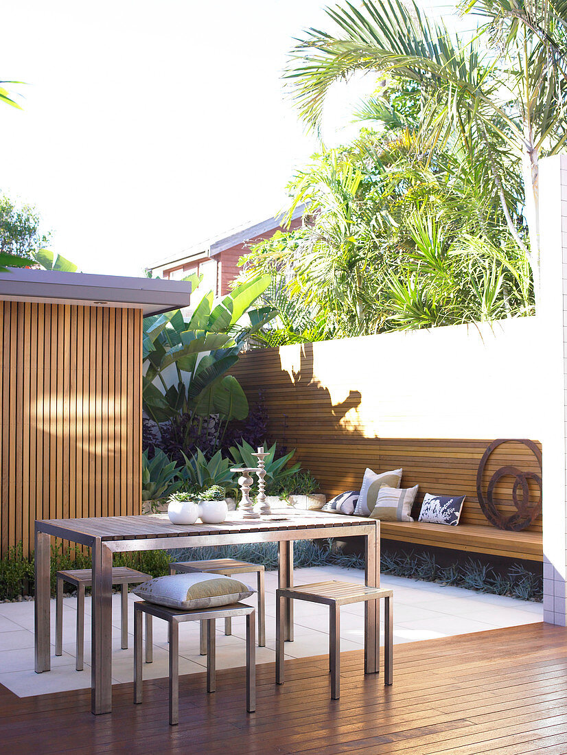 Stylish, sunny courtyard - modern terrace table and matching stools on floor with white tiles and wooden decking