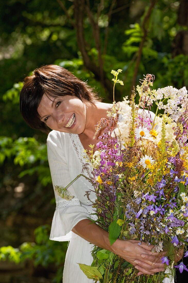 Woman holding armful of meadow flowers