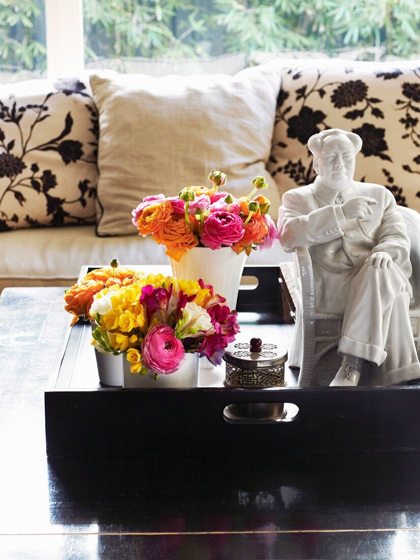 Blumenstrauss in Vasen neben weisser Porzellanfigur auf Tablett und Couchtisch vor Sofa mit geblümten Kissen