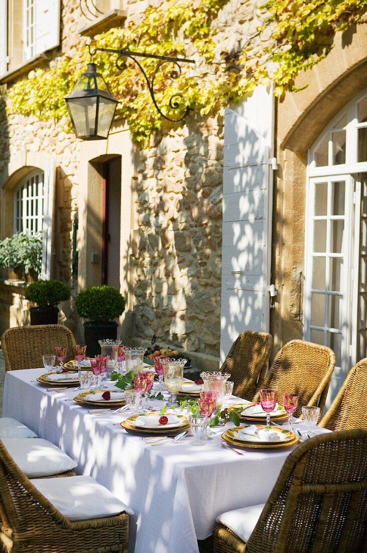 Festlich gedeckter Tisch auf sonnenbeschienener Terrasse vor mediterranem Landhaus