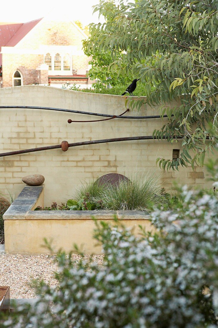 Curved brick wall with artistic decorations behind stone bench and raised bed
