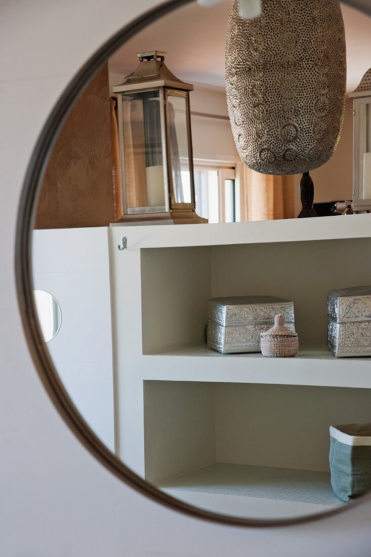 Decorative, Oriental metal boxes on shelves reflected in round mirror