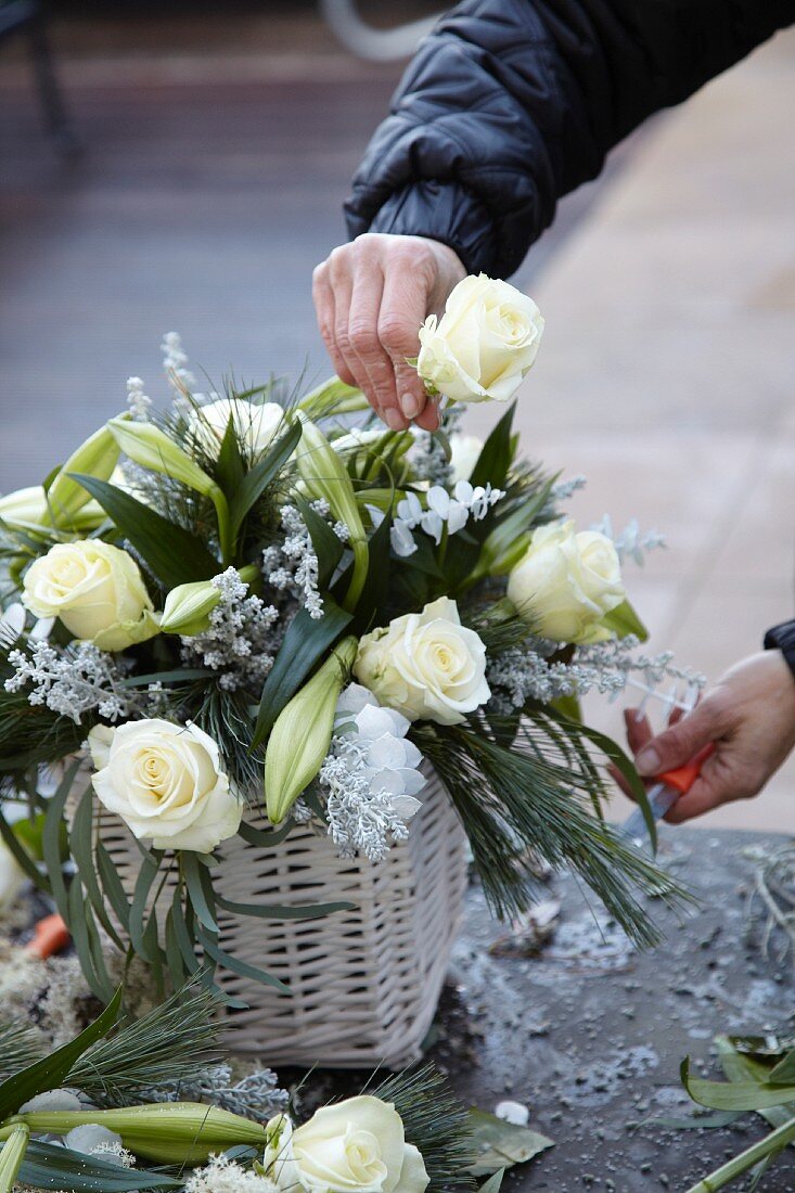 Hands placing white rose in almost-finished flower arrangement