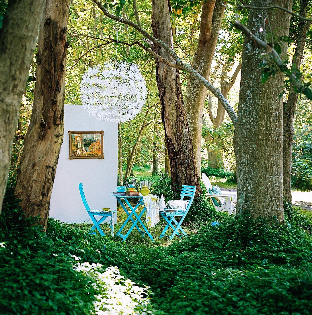 Gedeckter Gartentisch zwischen Bäumen im Park, daneben Trennwand mit Gemälde