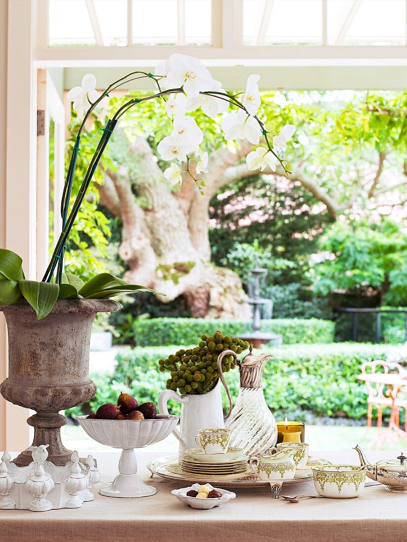 Blick in den Garten über gedecktem Tisch mit antikem Teegeschirr, handgefertigter Keramik und Orchidee