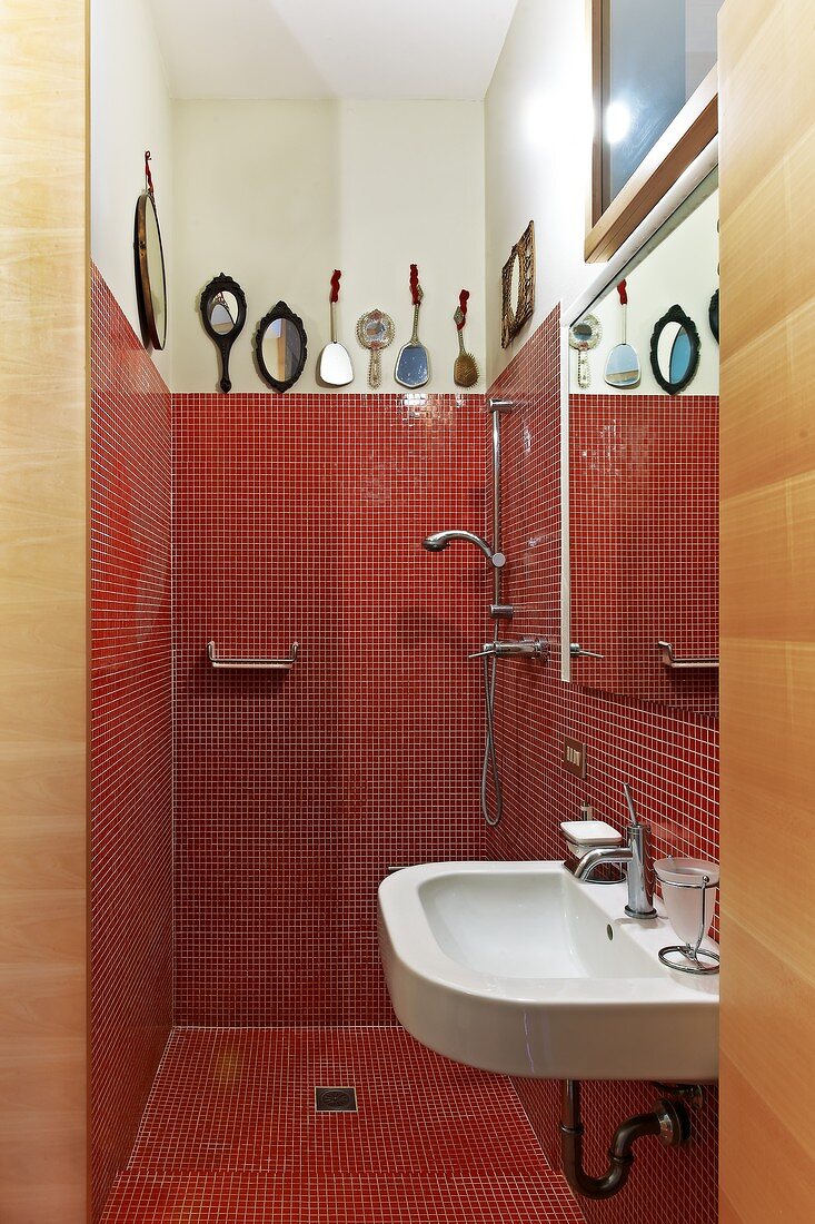Badeinblick - rote Mosaikfliesen im Duschbereich und schlichtes Waschbecken unter Spiegel