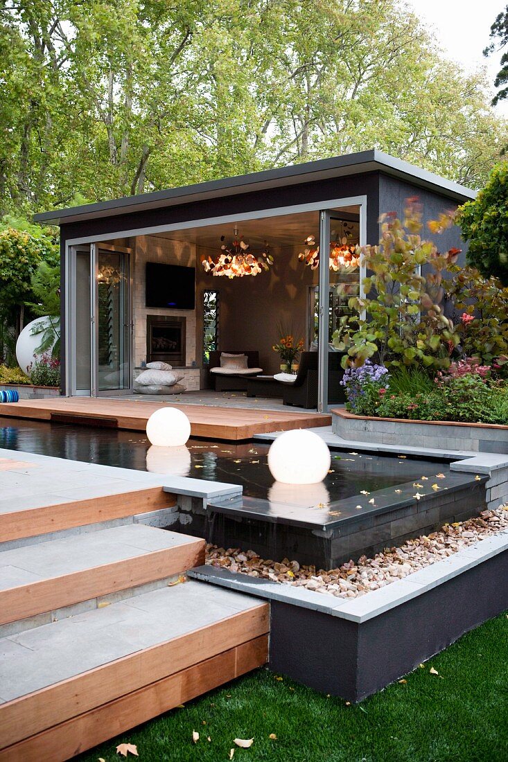 Terrassenanlage vor einem Wohnzimmer mit Holzdeck und Leuchtkugeln in einem Wasserbecken