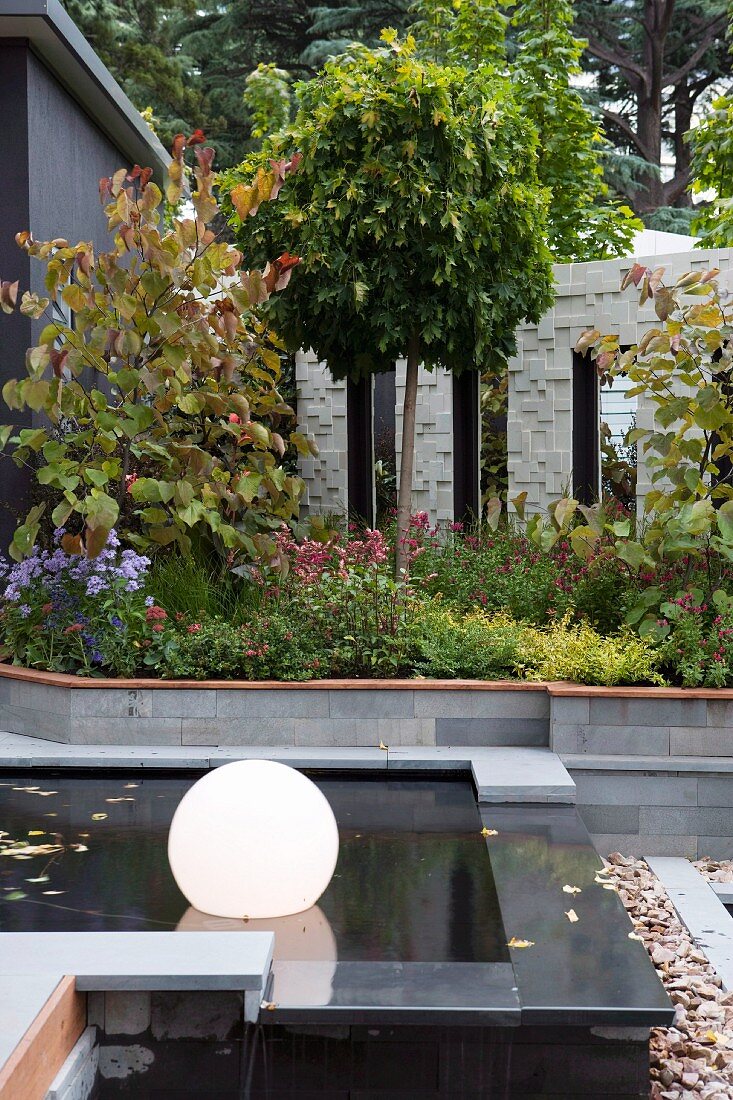 Courtyard garden with floating, spherical lamps in black pool and ornamental screen in background