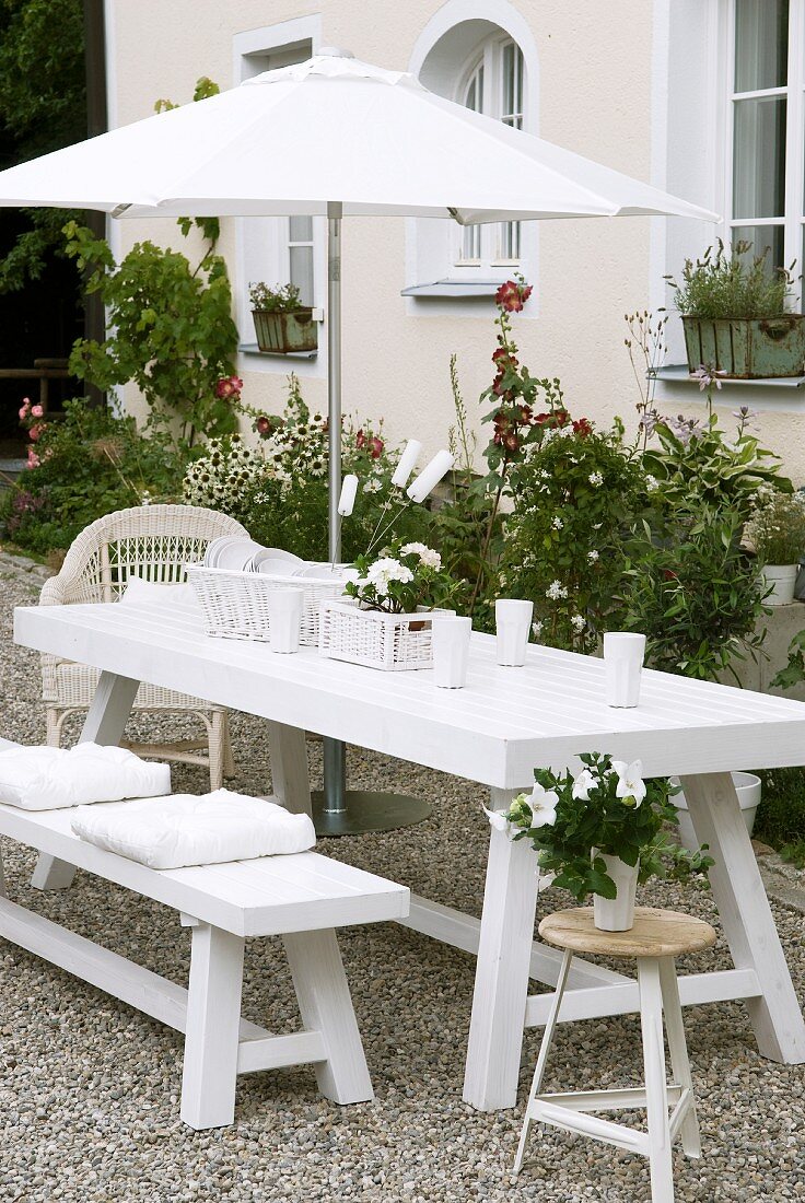 Weisser Picknicktisch mit Rattankörben und Porzellangeschirr im Garten