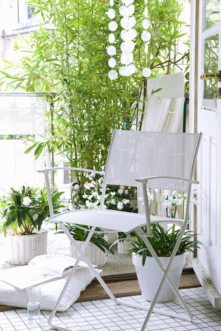 White folding chair in front of potted flowering plants and bamboo on balcony
