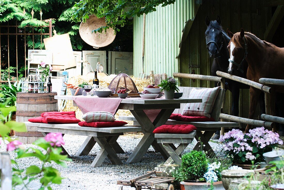 Rustic seating area with wooden benches, wooden table and cushions in front of stable