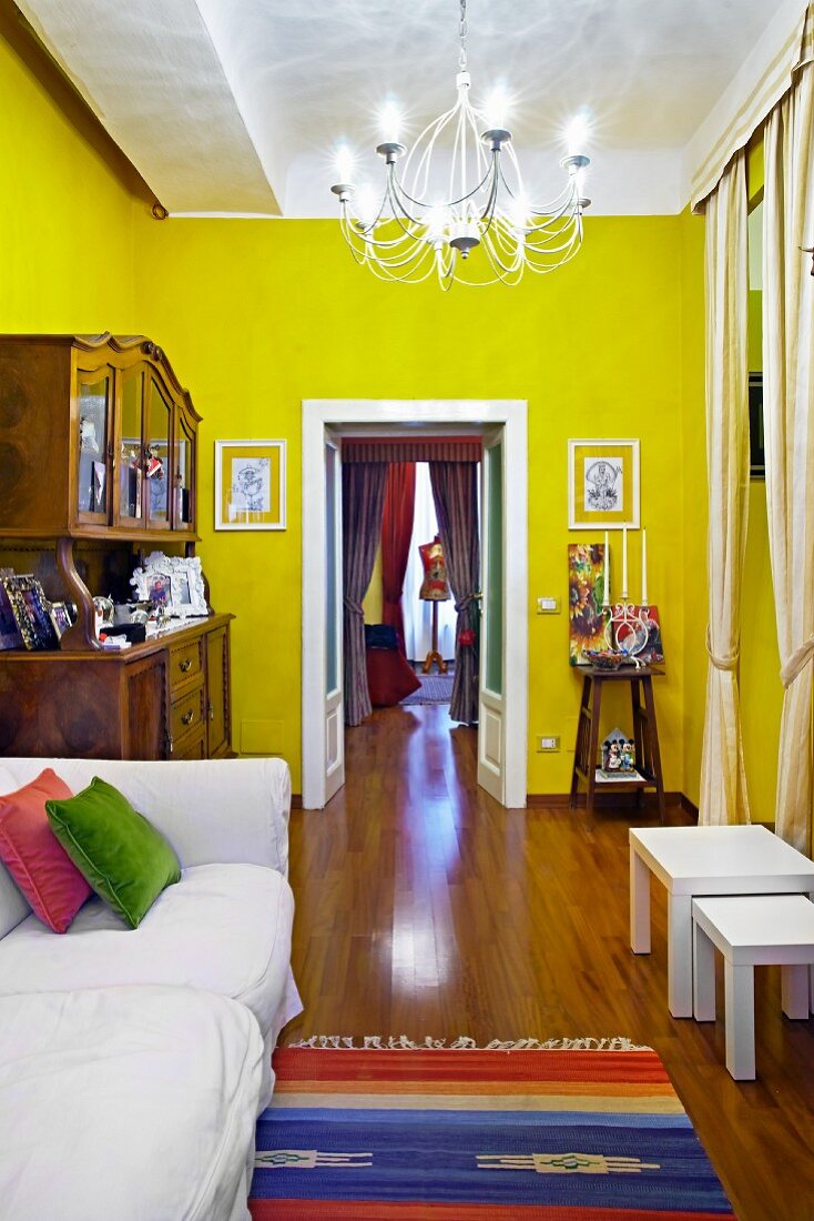 Weisses Polstersofa neben antikem Buffet und offene Flügeltür in einem gelb getönten Wohnraum