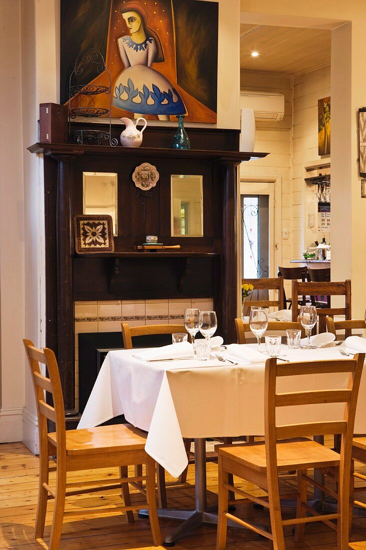 Restaurant tables in front of an open fireplace with antique wood surround and a modern painting above it