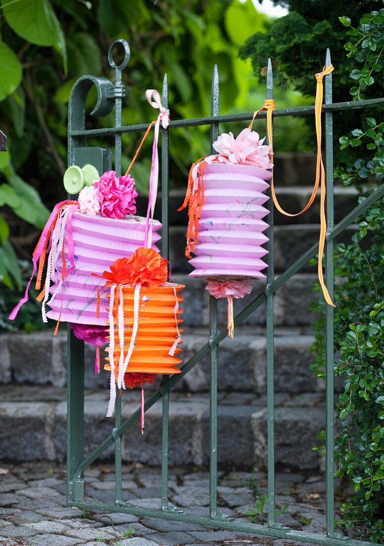 Mit Dekobändern, Papierblumen und Papierstreifen dekorierte Zuglaternen hängen am Gartentor
