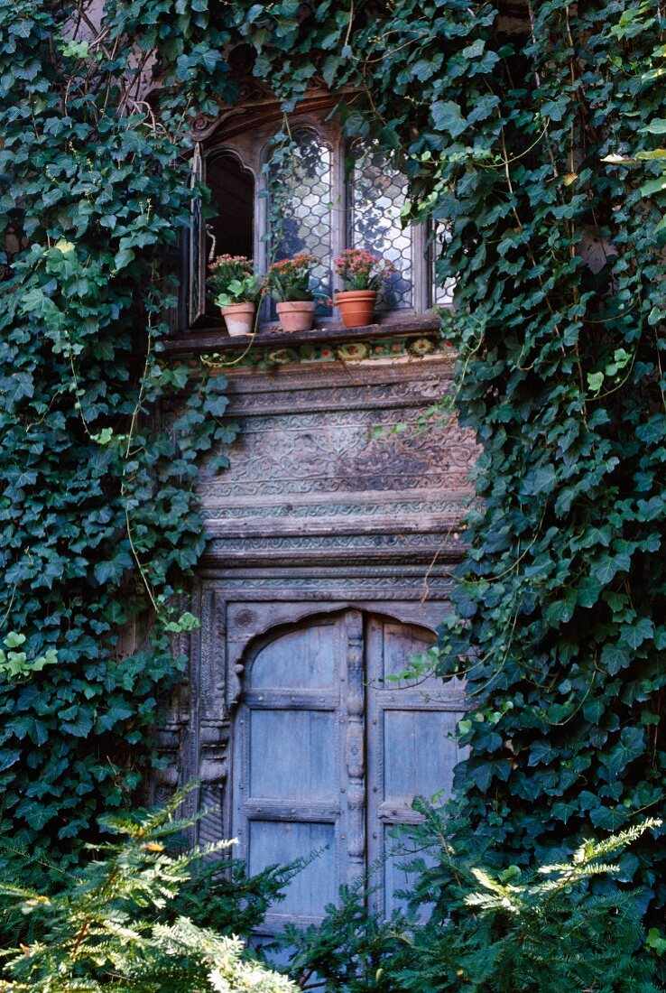 Efeuberankte Fassade eines traditionellen Landhauses mit dekorativ geschnitzen Fenstern