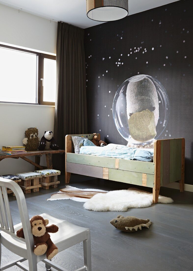 Kinderzimmerecke im Stilmix - Vintage Kinderbett vor dunkler Wand mit Weltall-Motiv und Stofftiere auf Stuhl und Boden