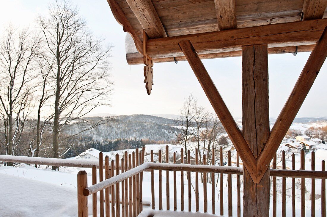Ausschnitt einer Holzstütze mit rustikalem Dachanschluss und Holzzaun in verschneiter Berglandschaft