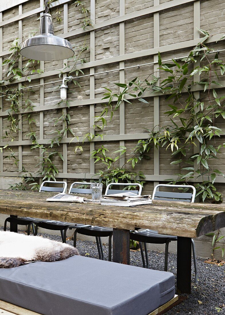 Tisch mit rustikalen Holzbohlen vor Holzwand mit Kletterpflanzen im Innenhof