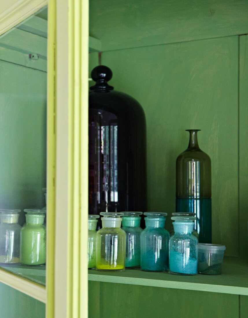 Verschiedene Färbemittel in Apothekerflaschen in einem grün angemalten Schrank