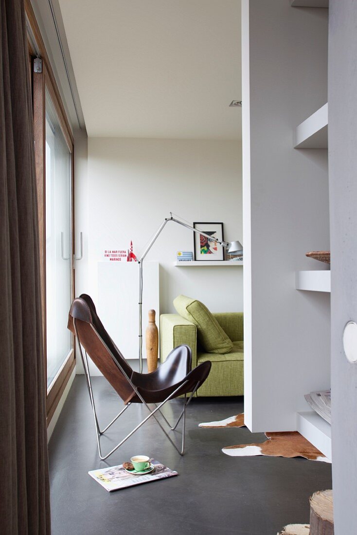 Lederner Fledermaussessel und lindgrünes Sofa mit Tolomeo-Stehlampe in modernem Wohnraum mit poliertem Betonboden