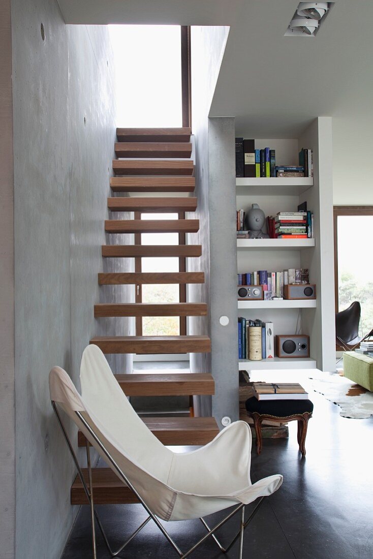 White butterfly chair in front of cantilever wooden steps of narrow interior staircase