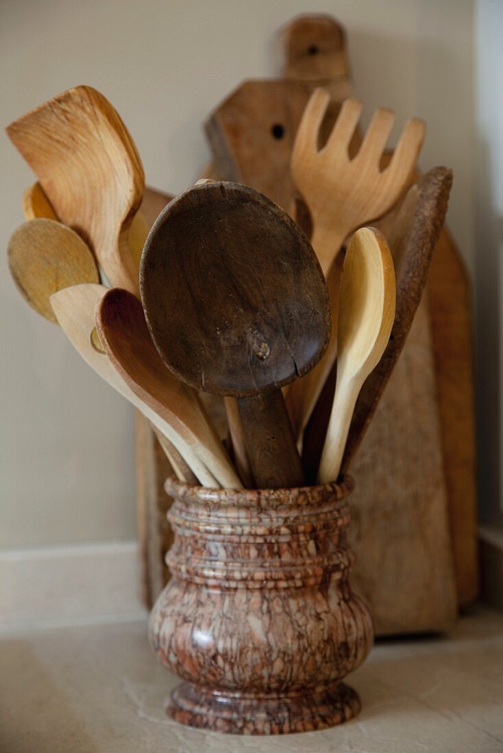 Collection of wooden spoons in stone pot and chopping boards in background