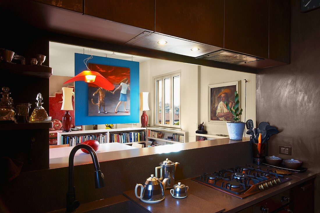 Küchenzeile im Halbdunkel vor offener Durchreiche und Blick ins Esszimmer auf blau getönten Raumteiler mit Bild