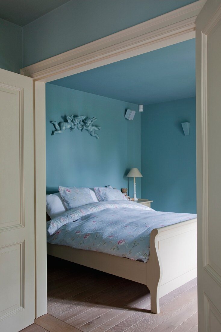 View into sky-blue bedroom with country-house-style double bed through open double door