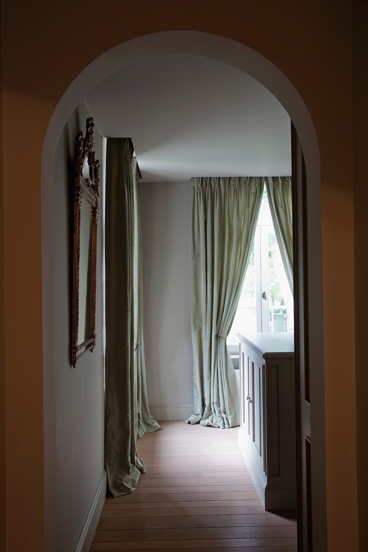 View though archway into interior with floor-length, gathered curtains on window