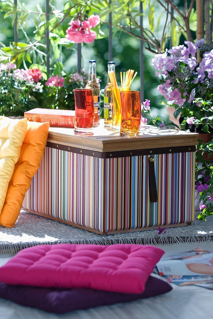 Gelbvioletter Farbklang für den Drink im Sommergarten - gestreifte Kühlbox und Sitzkissen vor blühendem Oleander und Phloxs