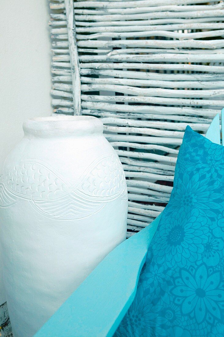 Pale ceramic floor vase and blue cushion against panel of sticks