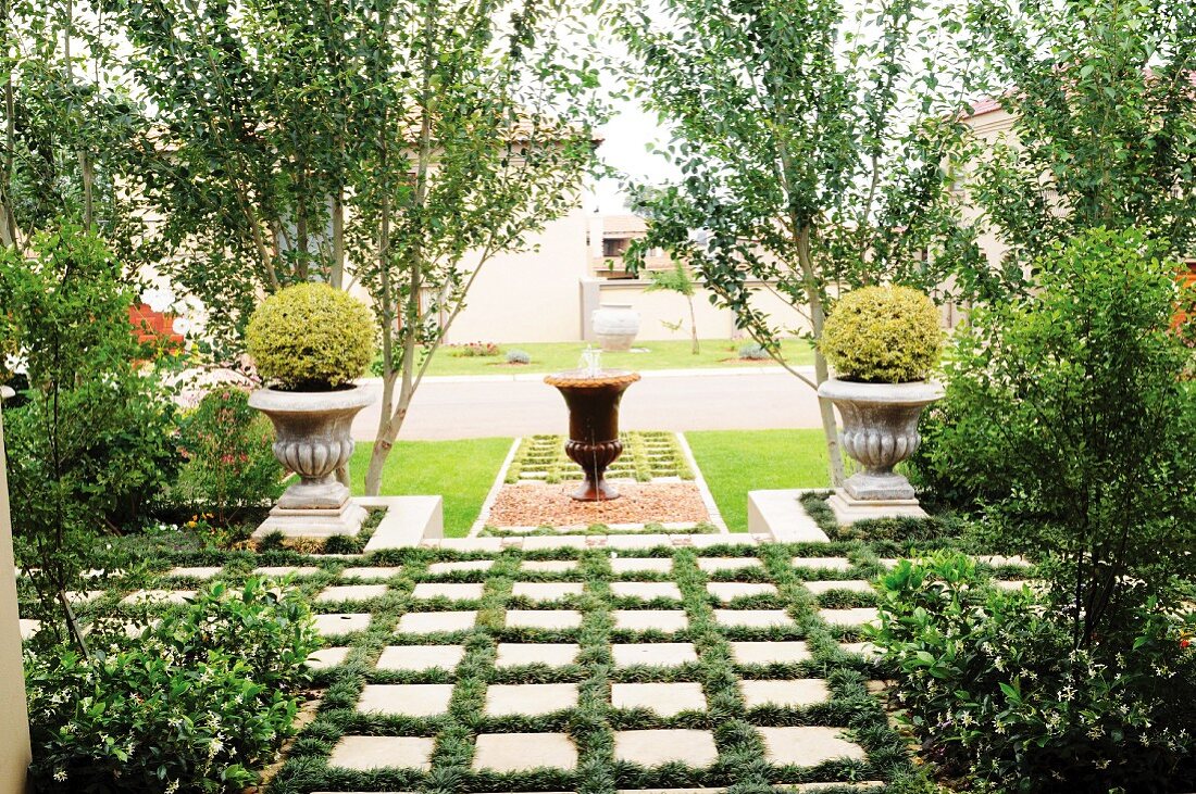 Amphoren im Antikstil vor Pappelreihe als Gestaltungselemente in einem Vorgarten; im Vordergrund mit breiter Rasenfuge verlegte Betonplatten