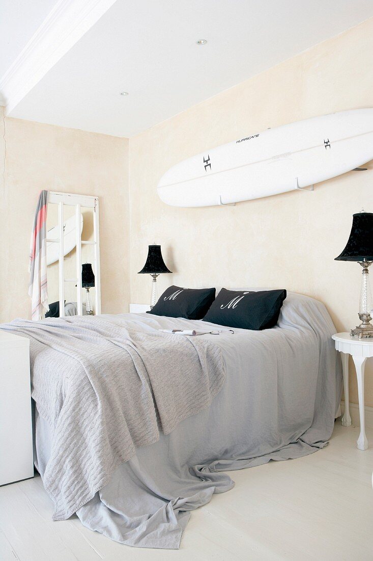 Doppelbett mit grauer Bettwäsche und an Wand befestigtes Surfbrett im Schlafzimmer