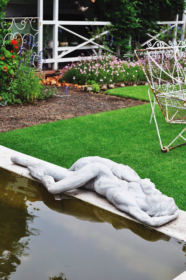Teich mit Betonumrandung und Statue im geordneten Garten