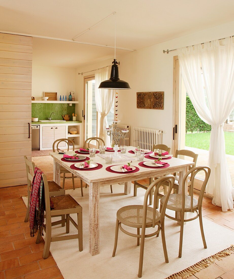 Bugholzstühle mit Sitzgeflecht und einfache Stühle mit Binsengeflecht an festlich gedecktem Tisch vor drapierten Vorhängen