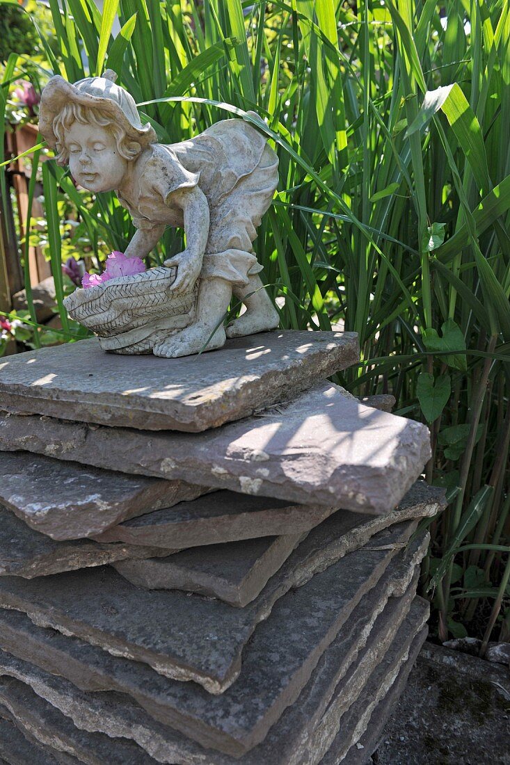 Kleine Steinfigur auf Stapel aus Natursteinplatten im Garten