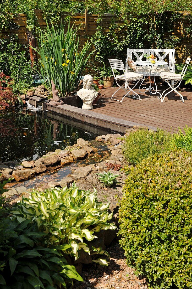 Kleiner Teich und Holzdeck mit Büste neben Tisch und Gartenstühlen