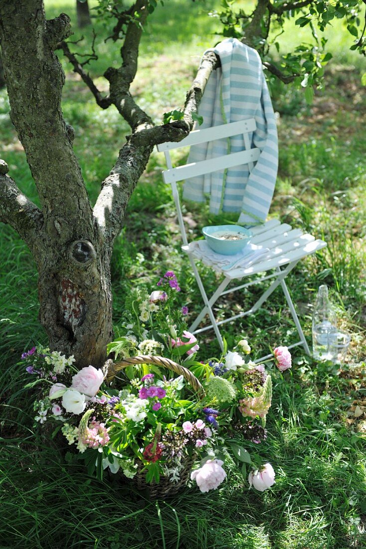 Basket of garden flowers on lawn and chair beneath tree