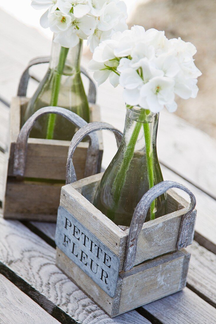 White flowers in water-filled bottles in wooden crates with handles
