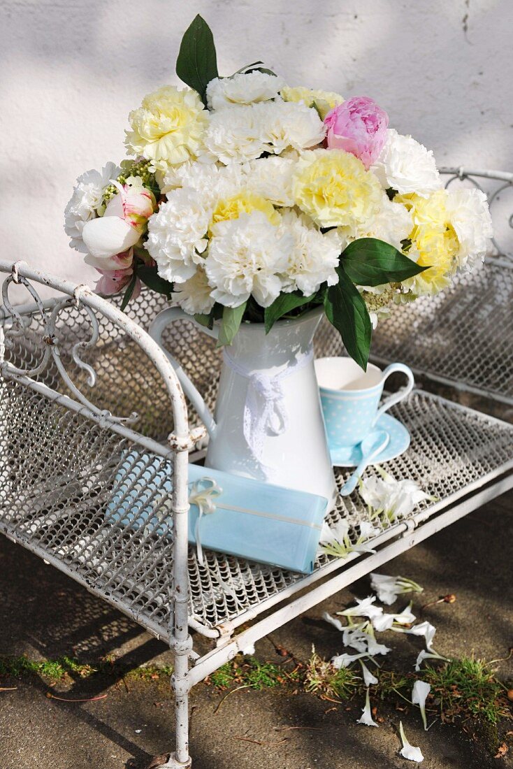 Bouquet of garden flowers in white case on white-painted wire mesh shelf