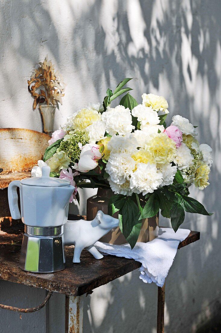 Gartenblumenstrauss und Espressokanne auf rostigem Tisch und Lichtspiel auf Wand