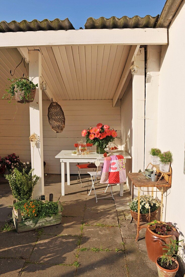 weiße holzverkleidete Loggia mit untergestelltem Tisch und Pflanzentöpfe auf sonniger Terrasse