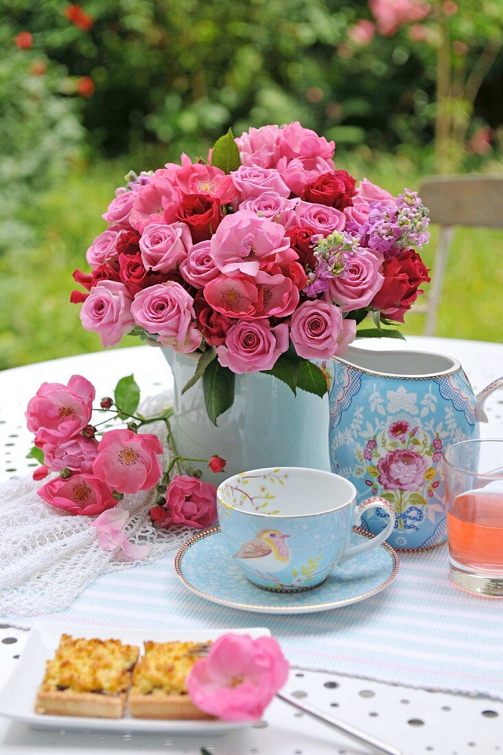 Kaffee und Kuchen im Garten mit Rosenstrauss in Porzellanvase