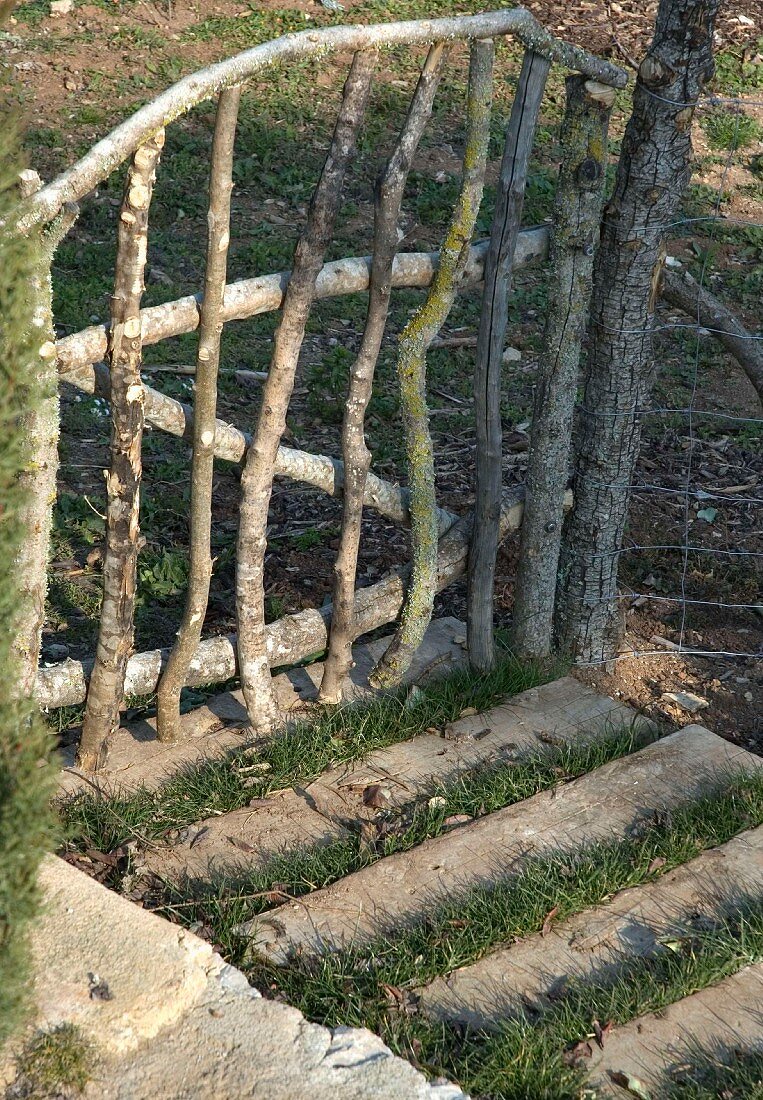Home-made garden gate of unfinished branches and stone blocks set into garden path
