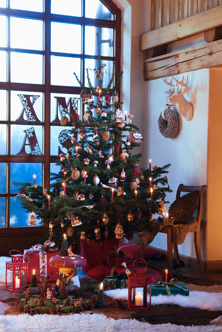 Decorated Christmas tree with lit candles in corner of room in front of floor-to-ceiling lattice window
