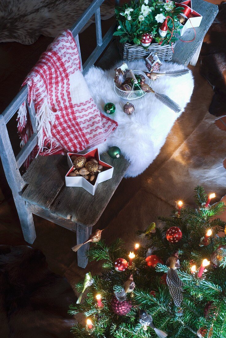 Christmas tree decorations and white fur rug on rustic bench next to decorated Christmas tree