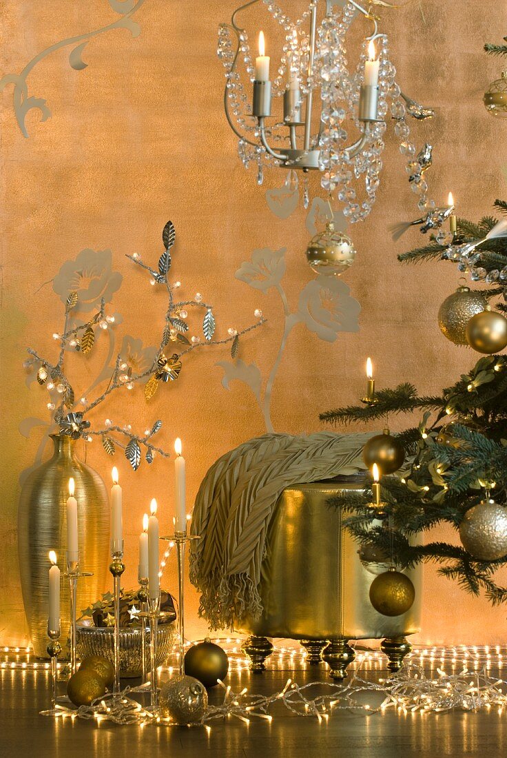 Gold Christmas decorations next to Christmas tree - fairy lights, candle arrangement, floor vase and stool